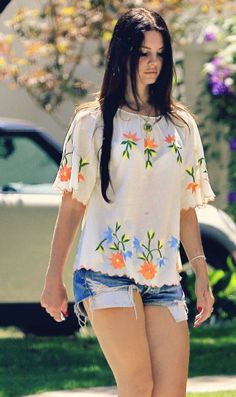 a young woman walking down the street in her short shorts and t - shirt with flowers on it