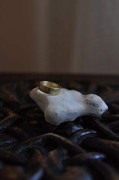 a gold wedding band sitting on top of a white piece of rock