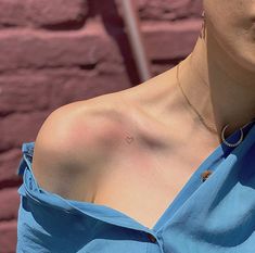 a woman wearing a blue shirt with a heart tattoo on her chest, standing in front of a brick wall