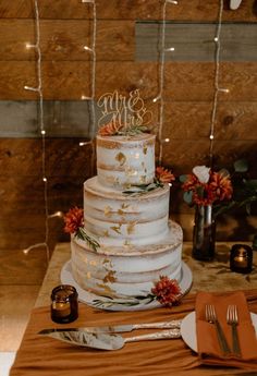 a wedding cake sitting on top of a wooden table next to candles and napkins