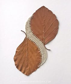 two brown leaves with white lace on them are laying next to each other in the shape of a leaf