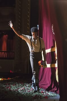 a man standing in front of a red curtain with his arms outstretched and flowers on the ground