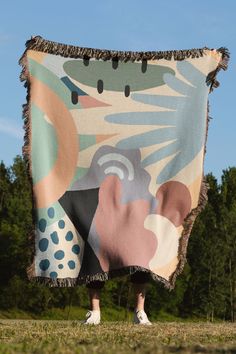 a person standing in the grass with a blanket on their back that has an image of flowers and leaves