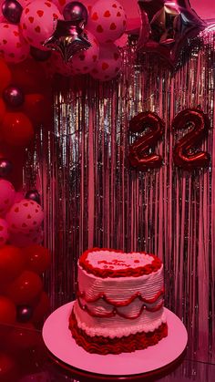 a red and white cake sitting on top of a table next to some balloons in the background