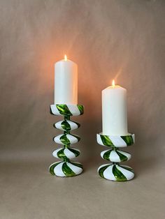 two white candles sitting next to each other with green leaves on them and one candle in the middle