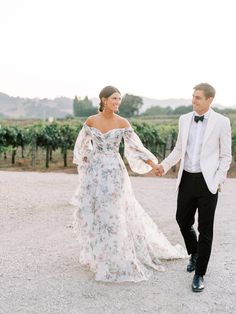 a bride and groom holding hands walking through the vineyard