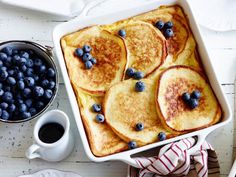 blueberries and pancakes in a white dish next to a cup of coffee