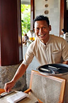 a man standing next to a pan on top of a wooden table with utensils in it