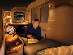 a woman sitting in an airplane reading a book next to a table with a lamp on it