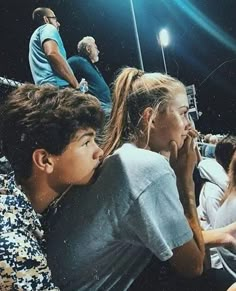 several people sitting in the stands at a baseball game and one person is holding his hand up to his mouth