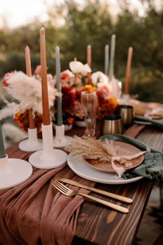 the table is set with candles, plates and napkins for an outdoor dinner party