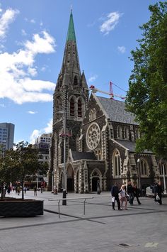 an old church with a green steeple and people walking around in the foreground