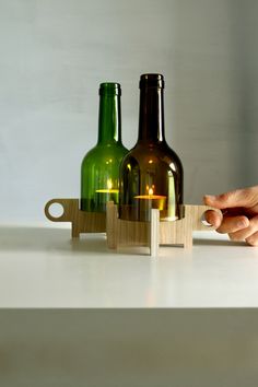 two green glass bottles sitting on top of a wooden block next to a candle holder