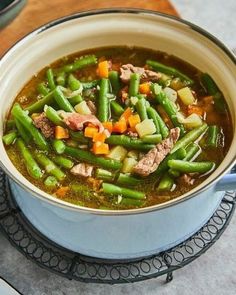 a bowl of soup with meat, green beans and carrots