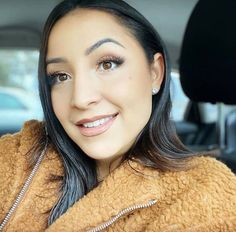 a woman sitting in the back seat of a car wearing a brown coat and smiling