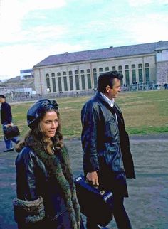 a man and woman walking in front of a building with a large white building behind them