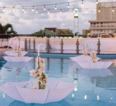 several umbrellas with flowers are floating in the pool at dusk or dawn, decorated with string lights and fairy lights