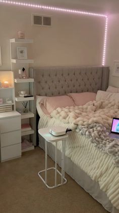 a laptop computer sitting on top of a bed next to a night stand and desk