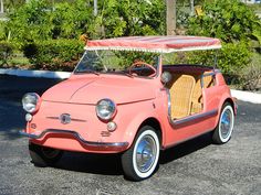 an old pink car parked in a parking lot next to some bushes and palm trees