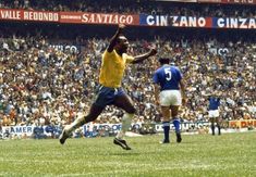 two men playing soccer in front of an audience at a sporting event, one is jumping up to catch the ball