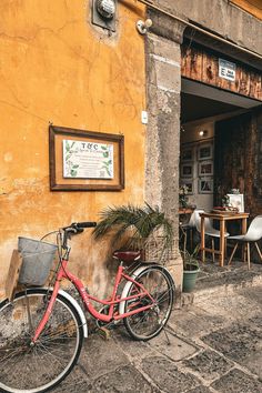 a red bike parked in front of a yellow building next to a potted plant