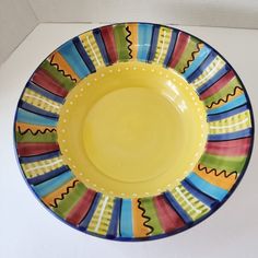 a yellow and blue plate with colorful designs on the rim is sitting on a white surface