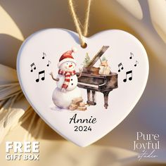 a white heart shaped ornament with a snowman playing the piano and music notes