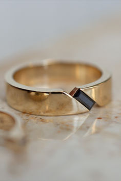 A gorgeous recent custom men's wedding band design, featuring a black moissanite baguette gemstone. The band is 14k yellow gold, and 5mm wide Mens Engagement Rings With Diamonds, Mens Wedding Rings Black And Gold, Diamond Rings Mens For Men, Engagement Rings Guys, Simple Engagement Rings For Men, Mens Wedding Bands Gold And Black, Cool Engagement Rings For Men, Art Deco Mens Wedding Band, Diamond Wedding Ring For Men