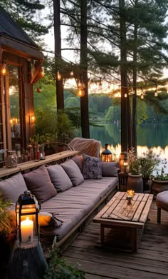 a deck with couches, tables and lights on it next to a lake in the evening