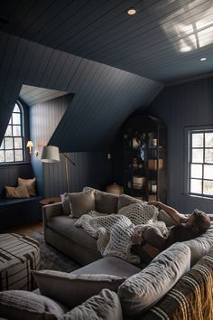 a woman laying on top of a couch in a living room next to a window