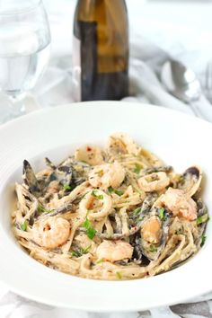 pasta with shrimp, clams and parsley in a white bowl next to a bottle of wine