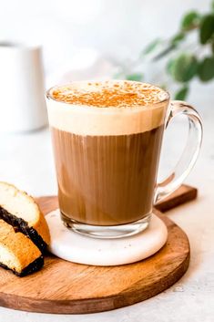 a cup of coffee and some bread on a wooden board next to a white mug