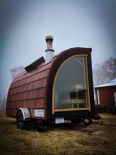 a tiny house made out of wood and metal with a chimney on the roof is parked in a field