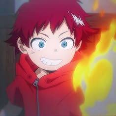 a young boy with red hair and blue eyes wearing a red hoodie in front of a fire