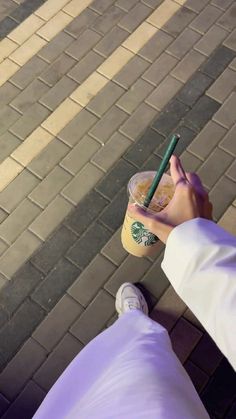 a person is holding a starbucks drink and looking down at their cell phone while standing on the sidewalk