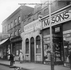 an old black and white photo of people walking down the street in front of shops