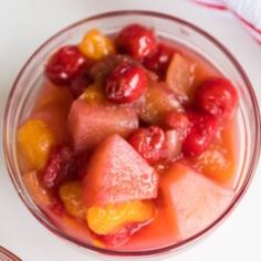 a glass bowl filled with fruit on top of a white table next to a spoon