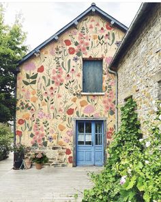 an old building with flowers painted on the side and blue door, surrounded by greenery