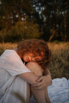 a woman with red hair is sitting in the grass and has her head on her hands