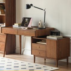 a wooden desk with two drawers and a lamp on top of it next to a book shelf