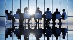 silhouettes of people sitting at a table in an office setting with the sun behind them