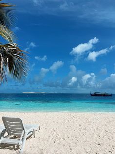 a beach with a boat in the water and a chair on the sand under a palm tree