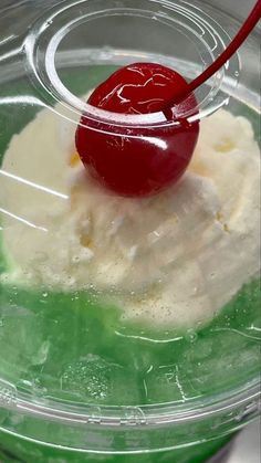 a red cherry sitting on top of ice cream in a plastic container with green liquid