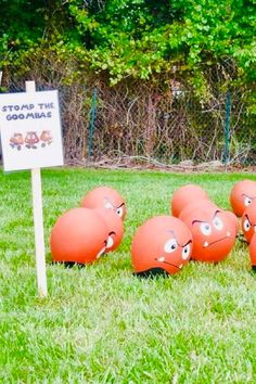 several orange balls with faces are in the grass near a sign that says stop the gophers