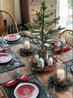 a table set for christmas with plates, candles and a small tree in the center