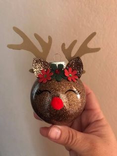 a hand holding a christmas ornament with reindeer antlers on it's head