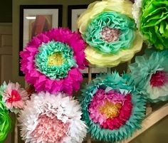 colorful paper flowers hanging on the wall in front of a staircase way with pictures behind them