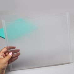 a hand holding a piece of clear acrylic on top of a white surface