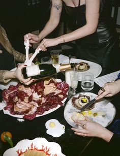 several people at a table with food and wine being poured on top of the plates