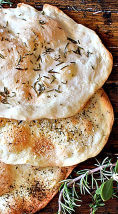 two pita breads with herbs and seasoning sitting on a wooden surface next to a sprig of rosemary